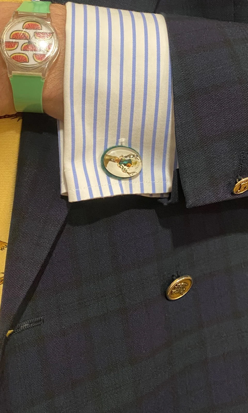 Ovaler Manschettenknopf mit Hirschmotiv und grünem Rand an einer blau gestreiften Manschette