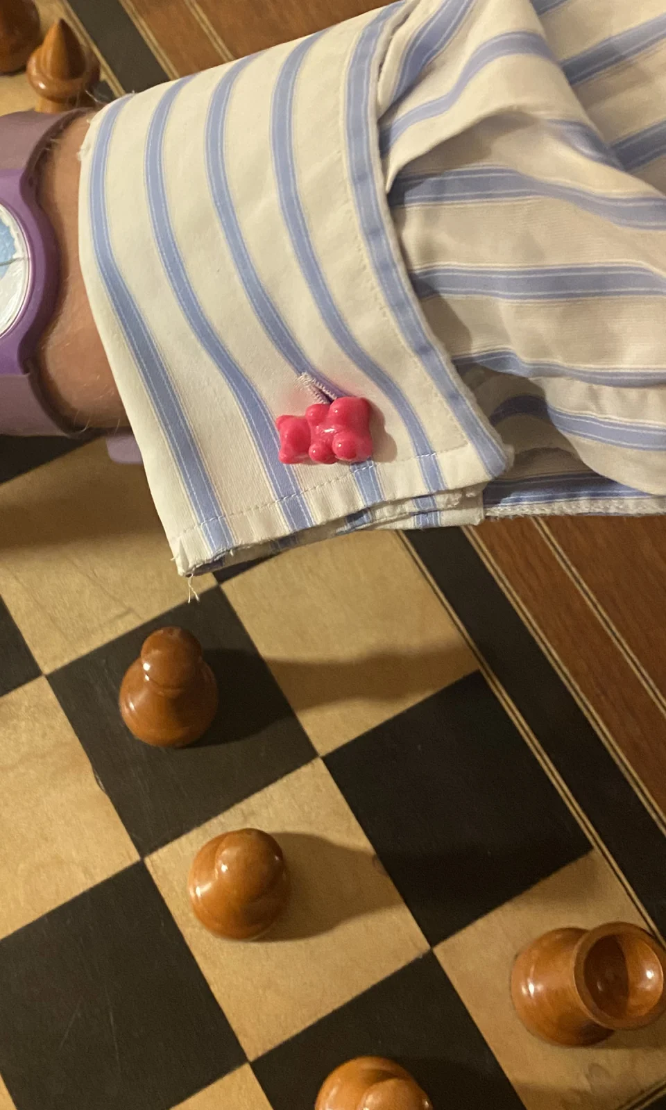 Manschettenknopf Manschettenbär in Pink an einer blau gestreiften Manschette über einem Schachbrett