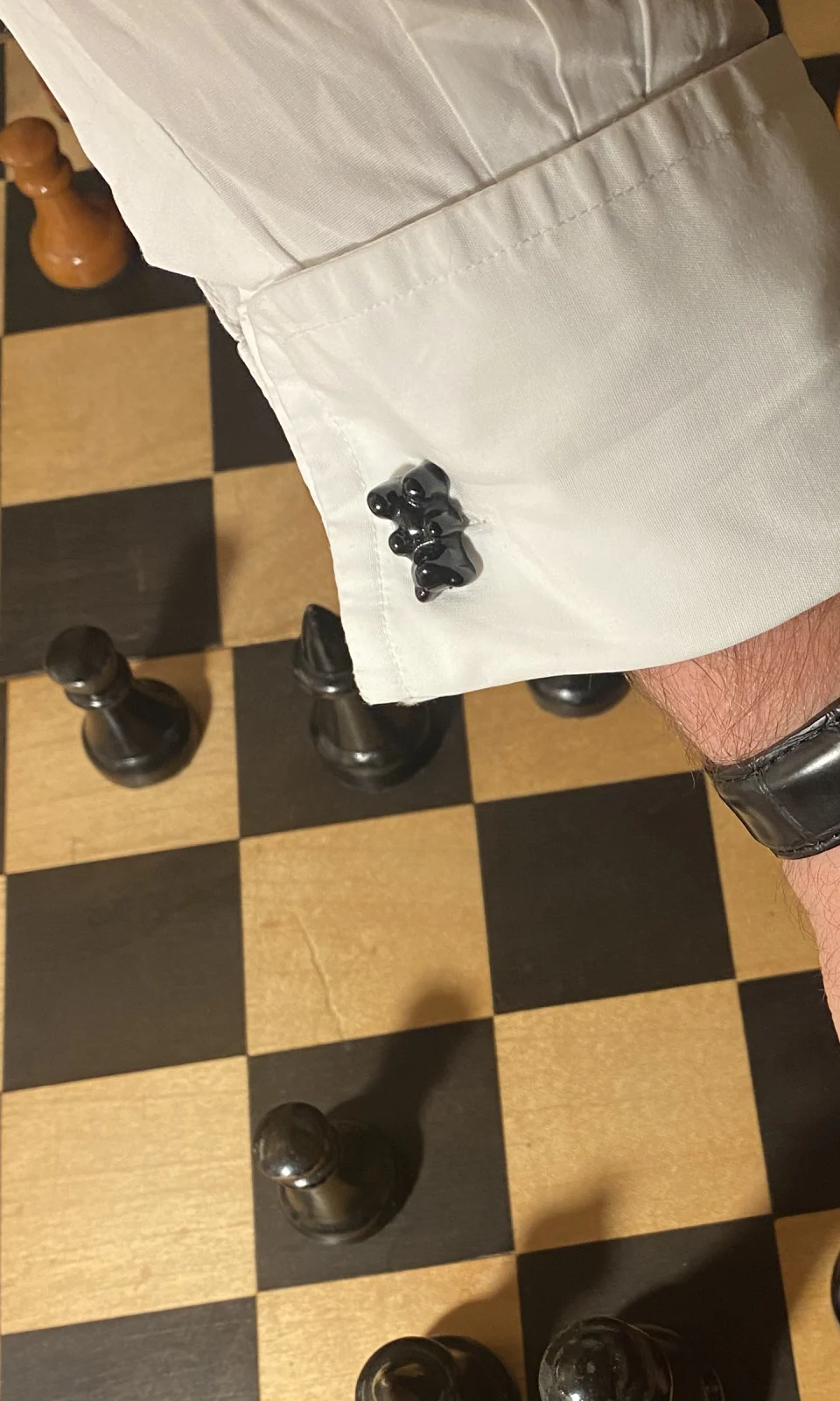 Manschettenknopf Manschettenbär in Schwarz an einer weißen Manschette über einem Schachbrett